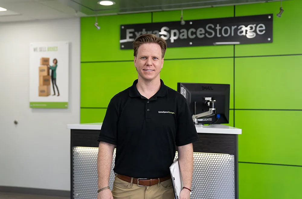 Man in black shirt stands at Extra Space Storage counter smiling