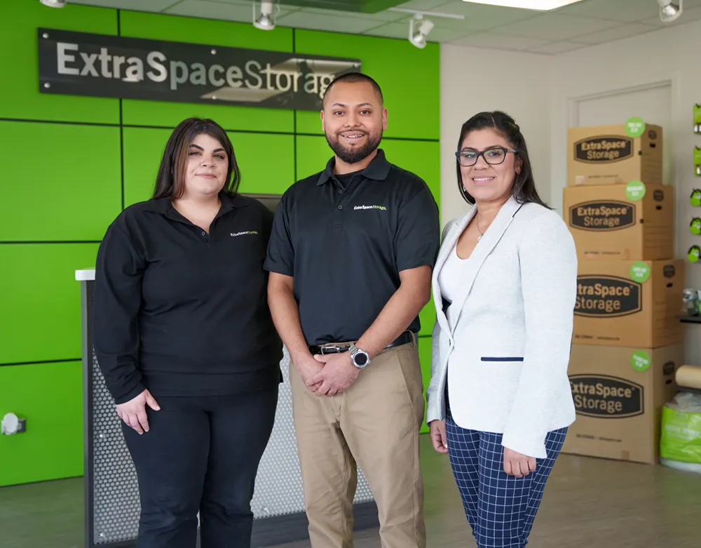 Three people stand in front of Extra Space Storage sign with boxes behind them.