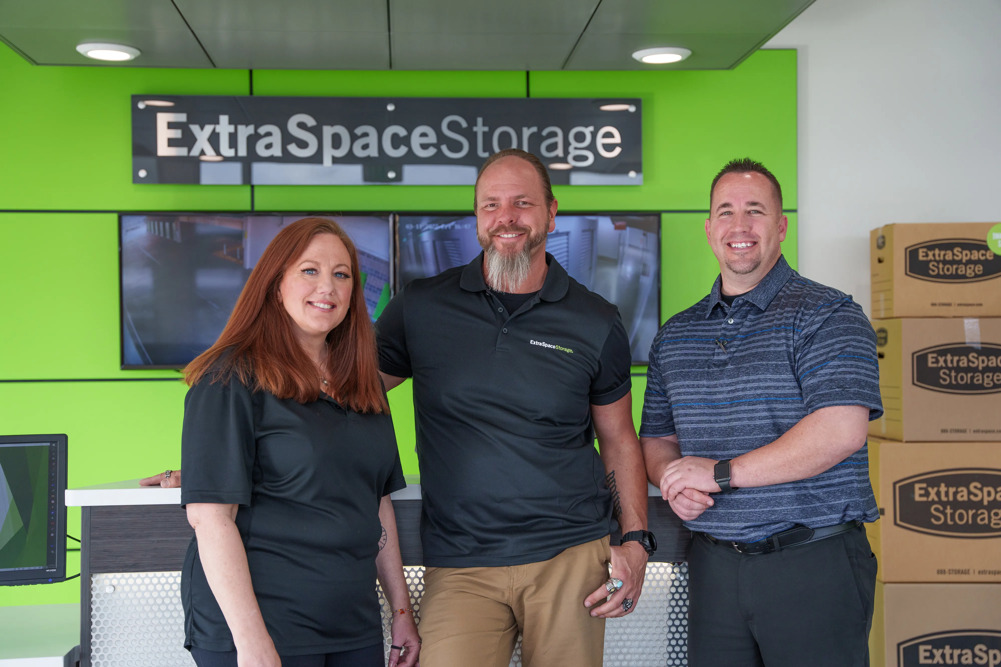 Three people stand in front of Extra Space Storage sign with boxes behind them