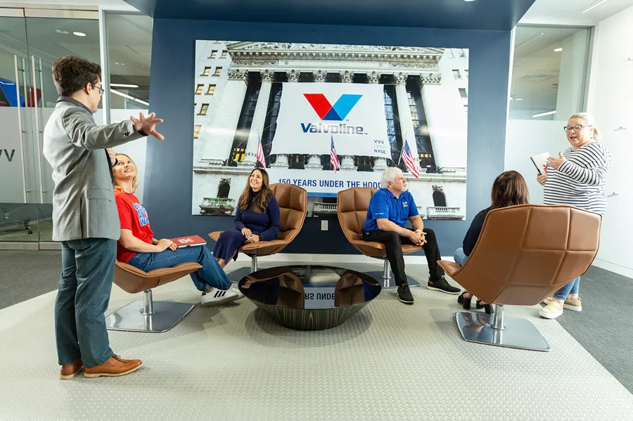 A diverse group of Valvoline employees is having an informal meeting in a modern lounge area.