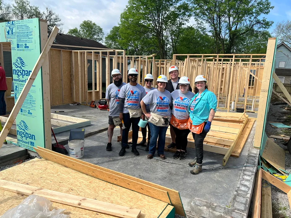 A group of Valvoline volunteers is smiling, wearing hard hats, at a Habitat for Humanity build site.