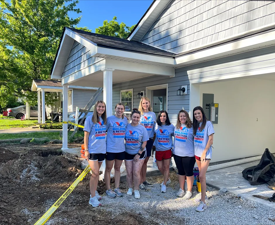 A group of seven smiling female Valvoline volunteers is posing at a house construction site.
