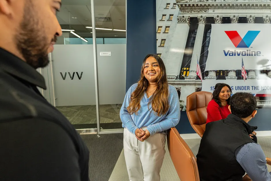 A smiling corporate employee is standing in a modern office near a Valvoline branded wall.
