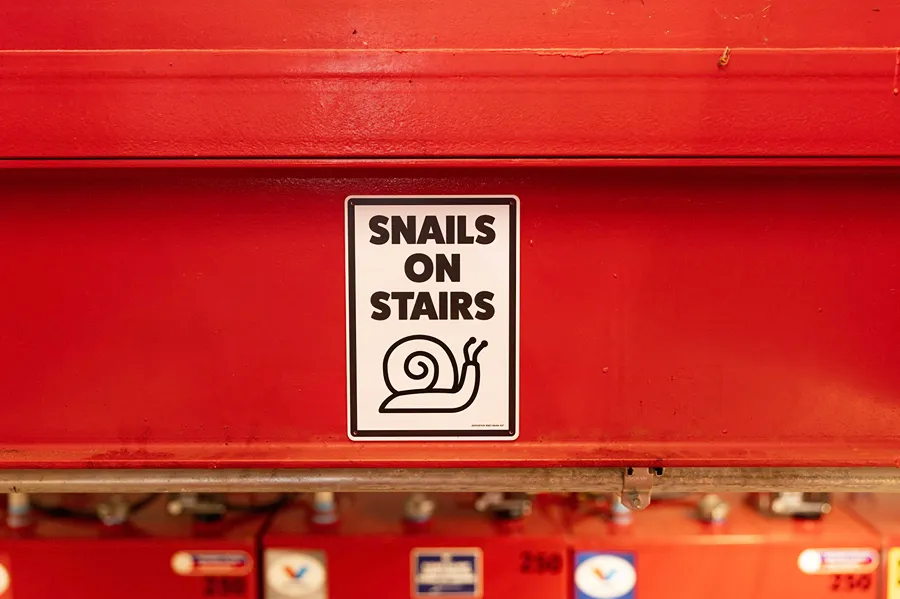 A close-up of a funny 'Snails on Stairs' safety sign on red equipment in a service bay.