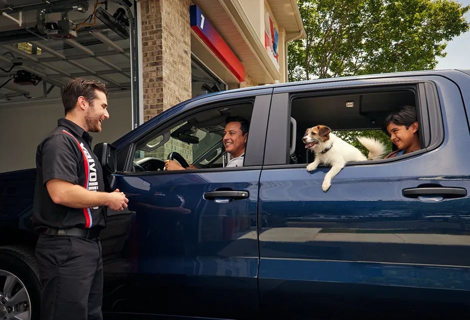 A **Valvoline technician** is greeting a smiling customer and his dog in a blue truck.