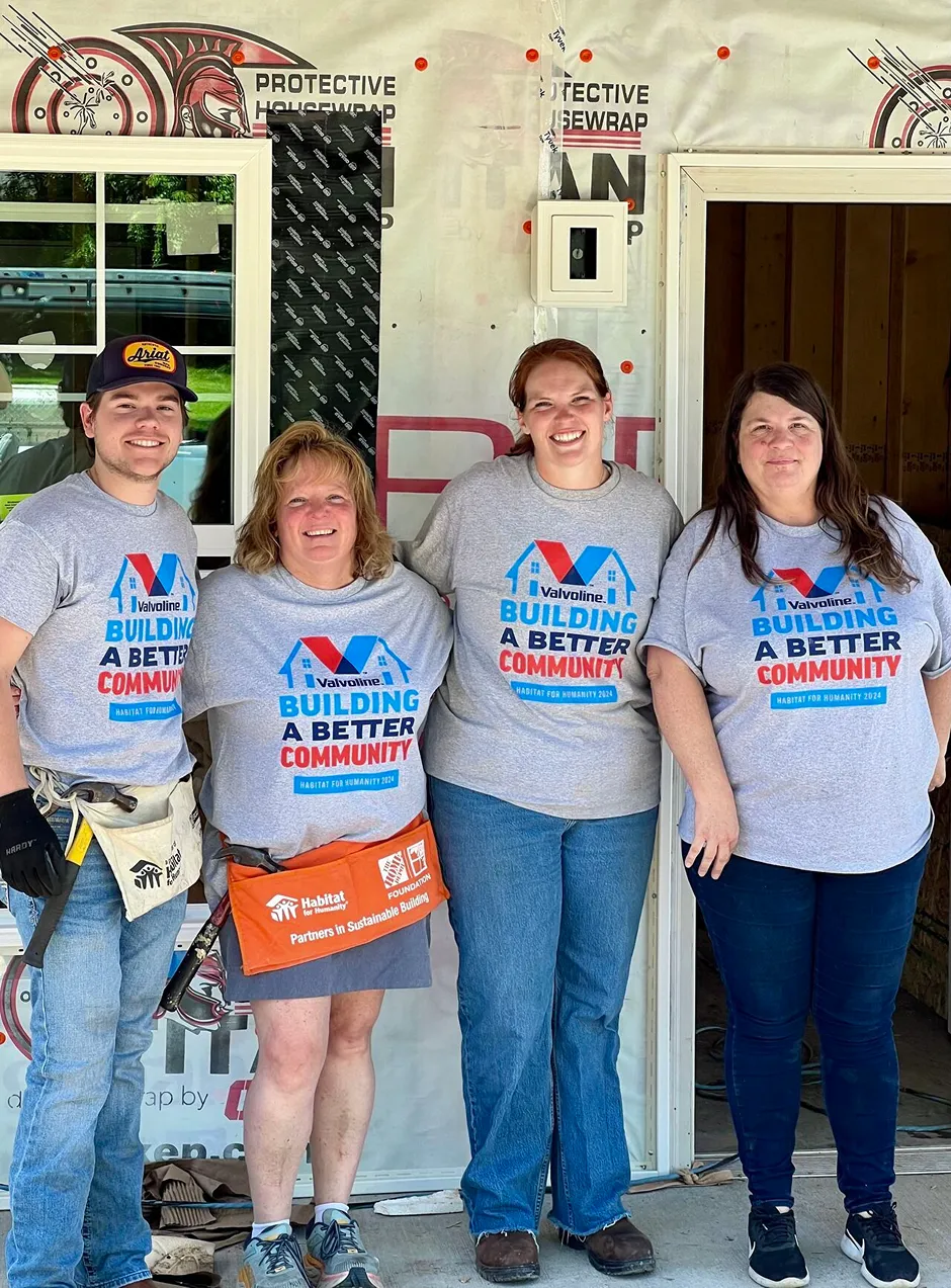 A group of four smiling Valvoline volunteers is posing in front of a house construction site.