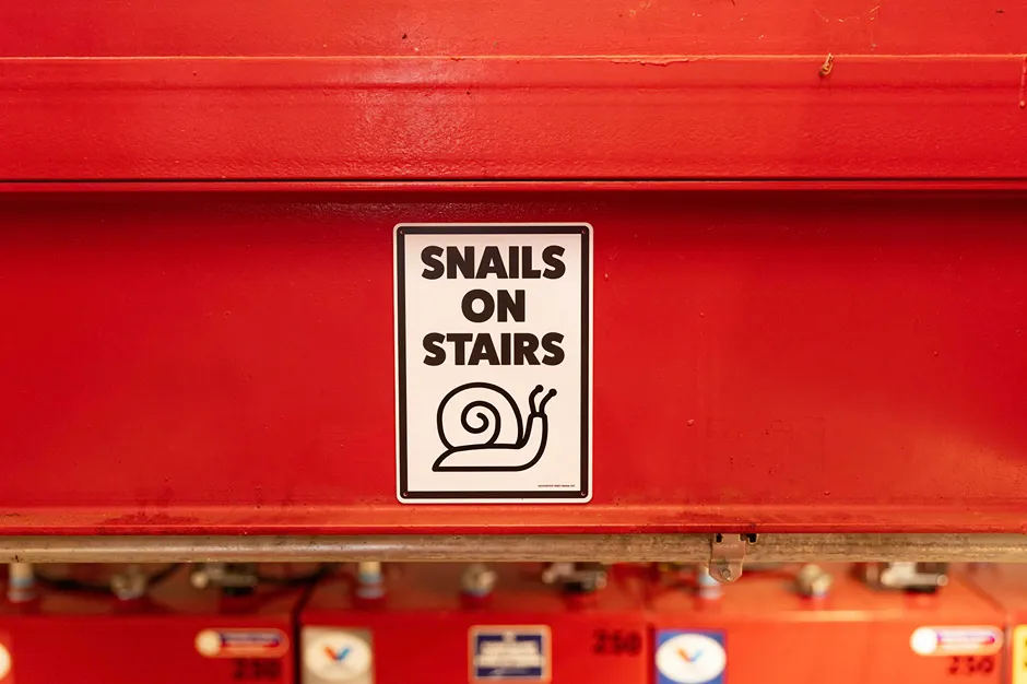 A close-up of a funny 'Snails on Stairs' safety sign on red equipment in a service bay.
