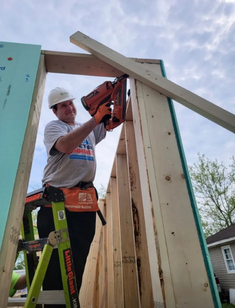 A Valvoline volunteer in a hard hat is using a nail gun to build a house frame.