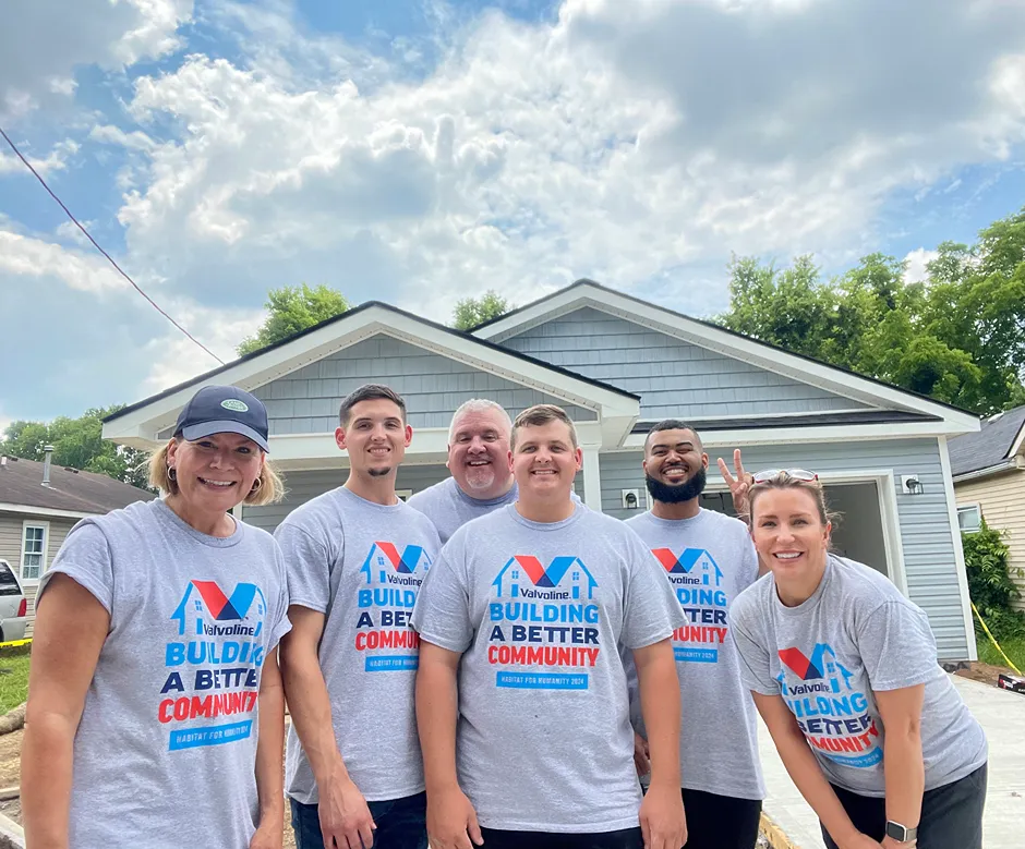 A diverse group of six smiling Valvoline volunteers is standing in front of a newly built house.