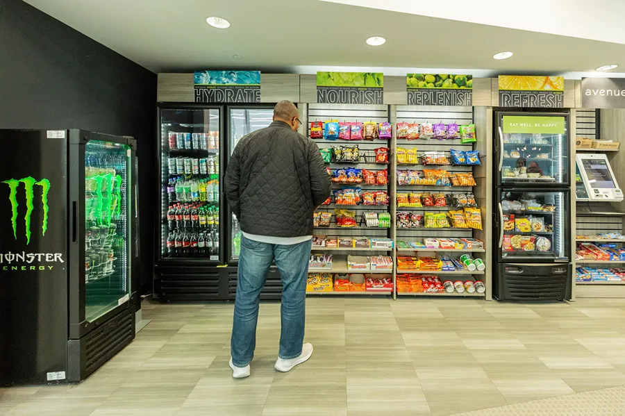 An employee is browsing snack and drink selections at an unattended micro-market in the office.