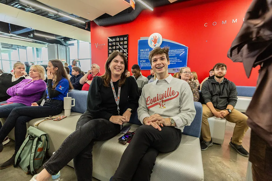 Two smiling employees are sitting together in the audience during a corporate event.