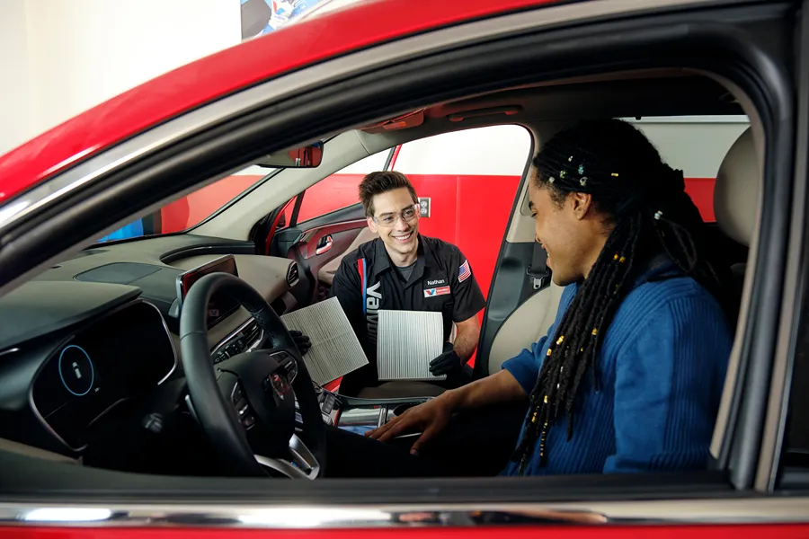 A smiling Valvoline technician is showing a customer a new air filter in their vehicle.
