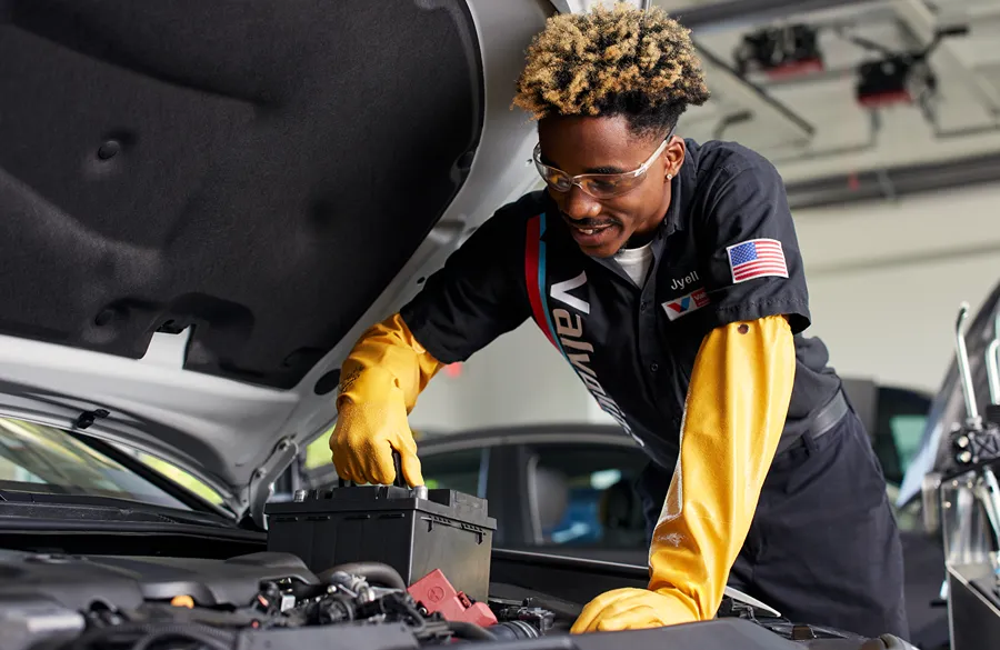 A smiling Valvoline technician is expertly replacing a car battery.