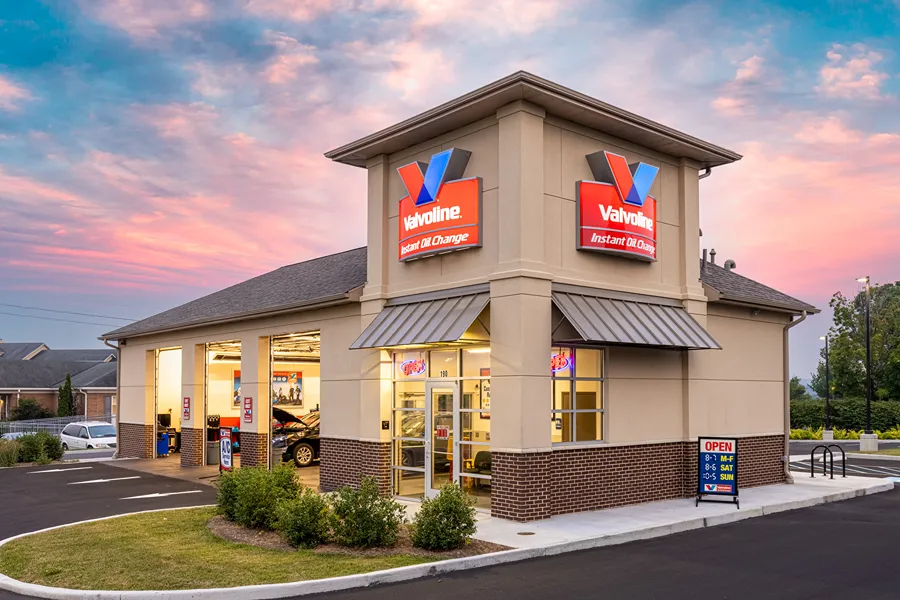 The modern exterior of a **Valvoline Instant Oil Change** store at sunset with bay doors open.