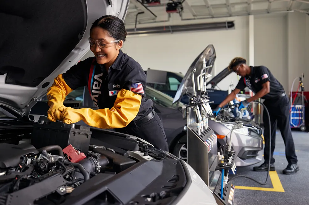 A smiling female Valvoline technician is expertly servicing a car engine in a clean bay.