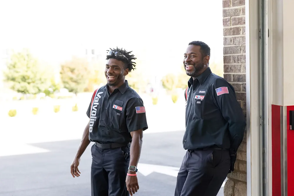 Two friendly Valvoline service center team members are smiling and relaxing outside the bay.