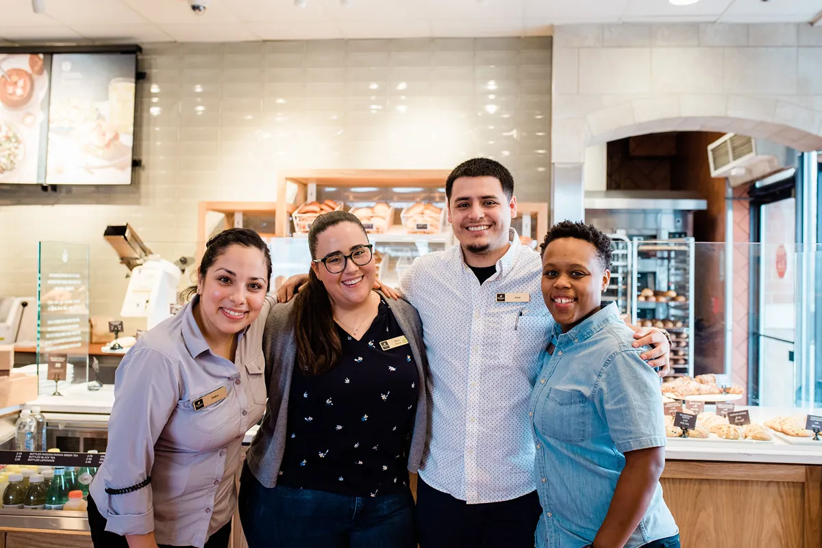 Four smiling employees posing together in a bakery setting