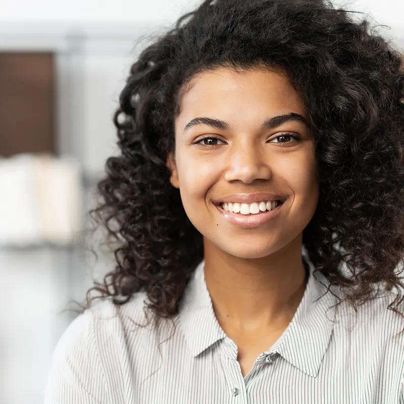 A smiling woman with curly hair wearing a striped shirt in a kitchen setting