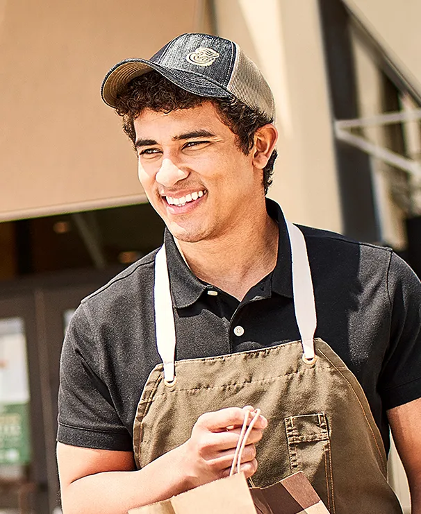 Smiling man in apron holding shopping bags outside store