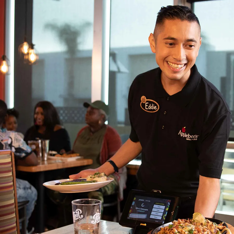 Applebee's server delivering food to smiling customers at a table, restaurant interior with warm lighting