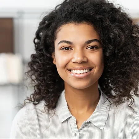 Smiling person with curly hair wearing a striped collared shirt in an office setting