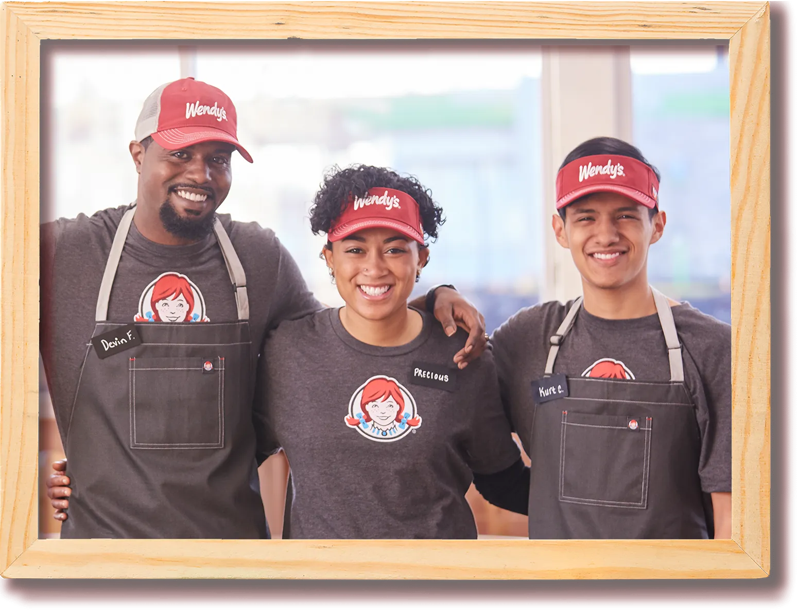 Three smiling Wendy's employees stand together wearing matching uniforms and hats