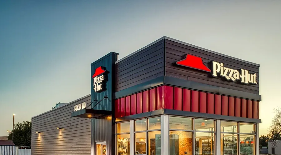 Exterior of a modern Pizza Hut restaurant at sunset, showing branding and pick-up area.