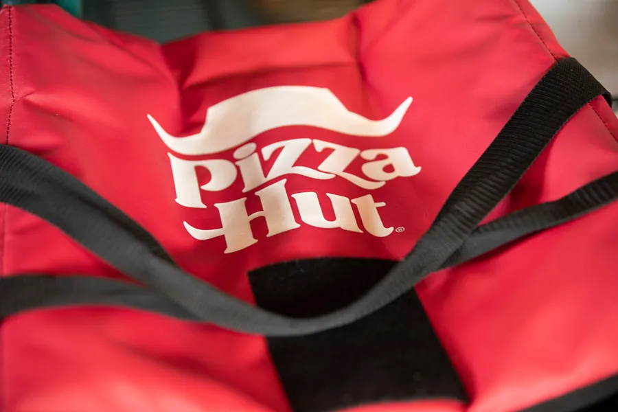 Close-up of a red Pizza Hut insulated delivery bag with the company logo and black straps.