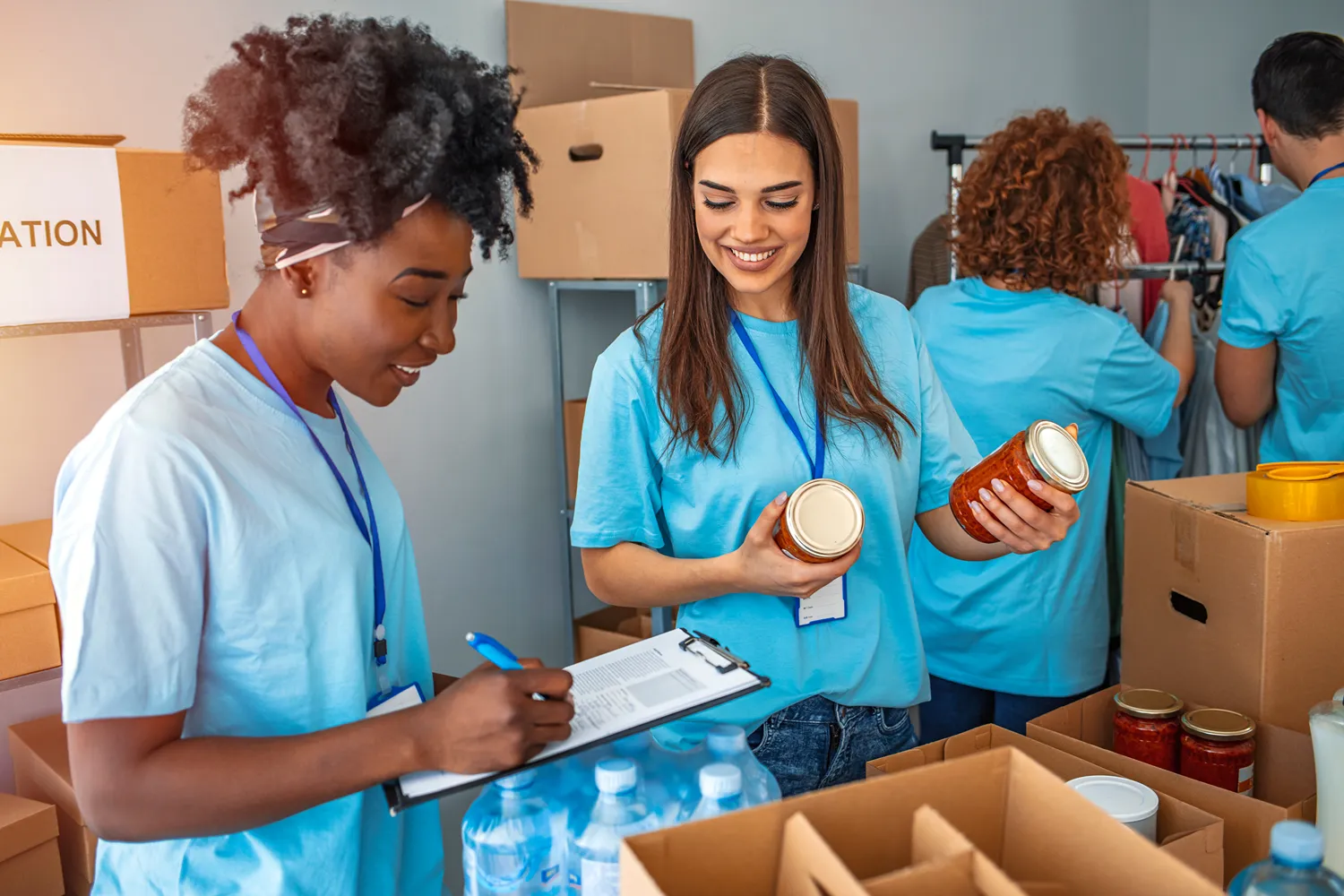 Two volunteers in blue shirts organize food donations in a community center