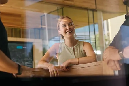 Three smiling colleagues conversing through a glass window in an office