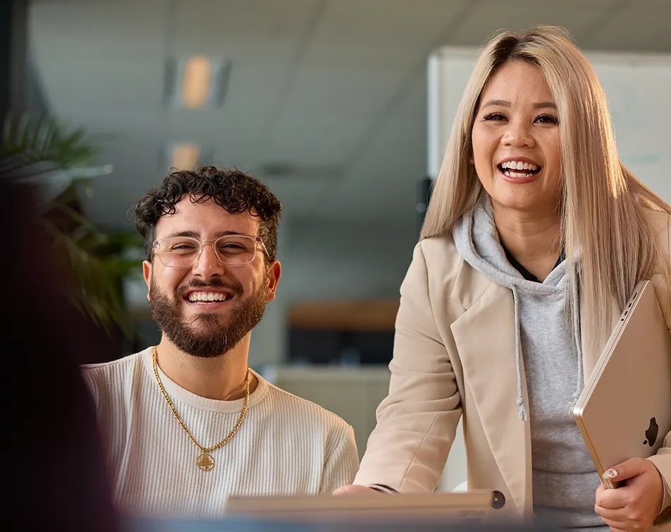 Two smiling colleagues working on laptops in a modern office