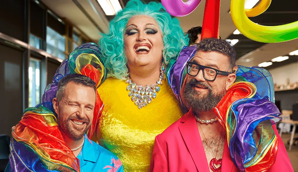 Three people smiling, one in drag, wearing colorful and rainbow attire