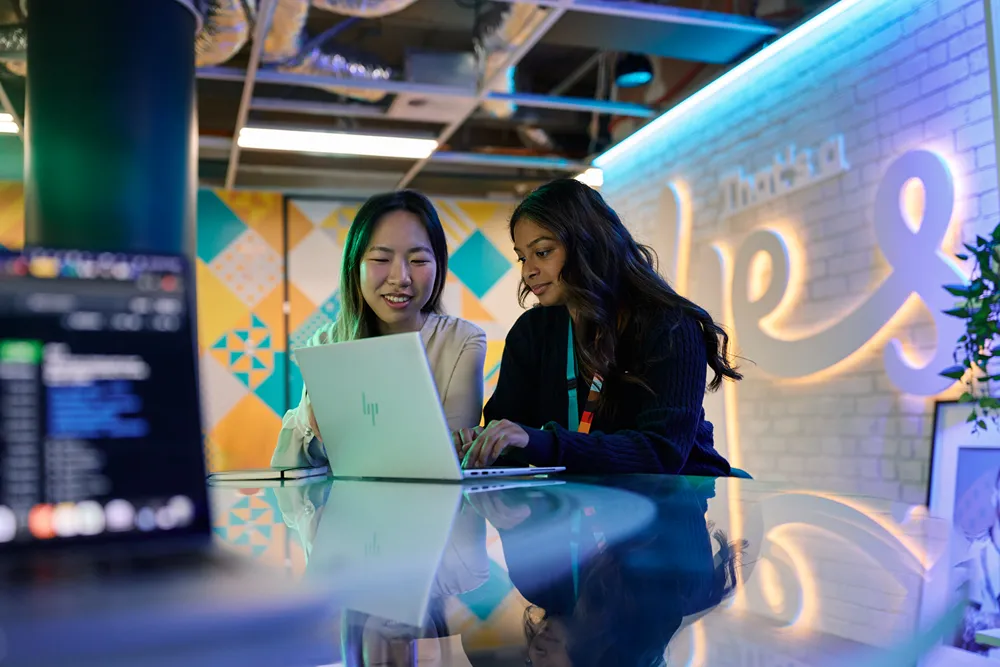 Two young women collaborating on a laptop in a modern office