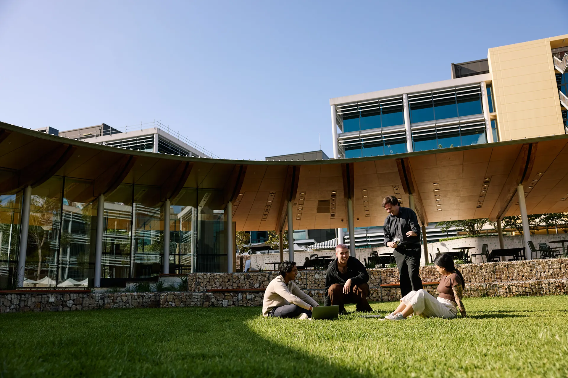 Four people gathered on a sunny lawn outside a modern building