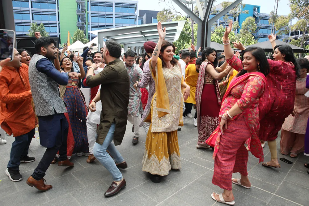 A group of diverse people in traditional Indian attire happily dancing outdoors at a cultural event