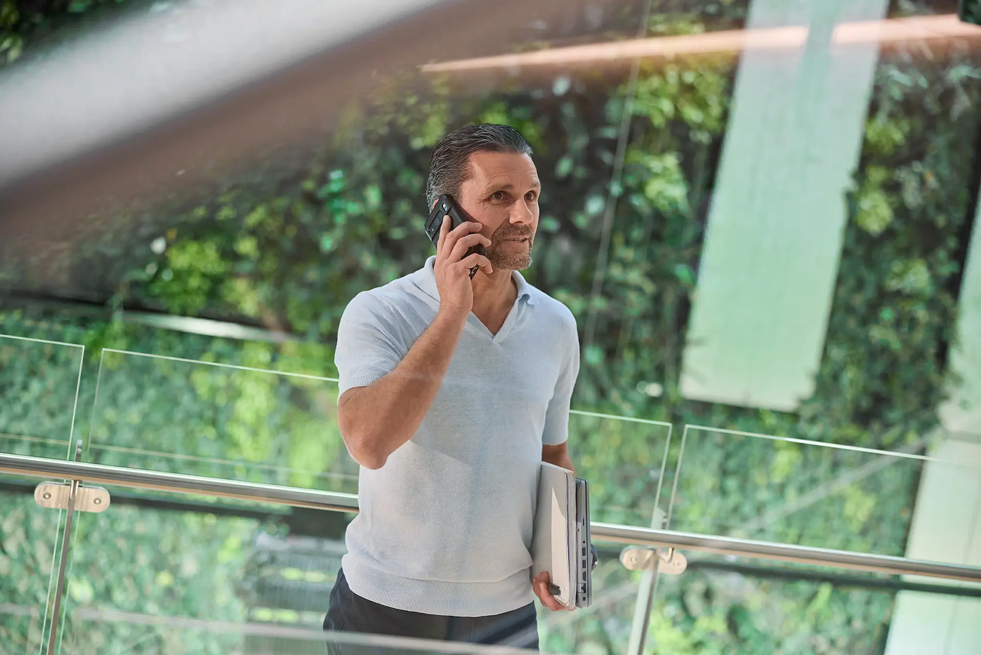 A man talking into his phone with one hand and the other holding a laptop and papers