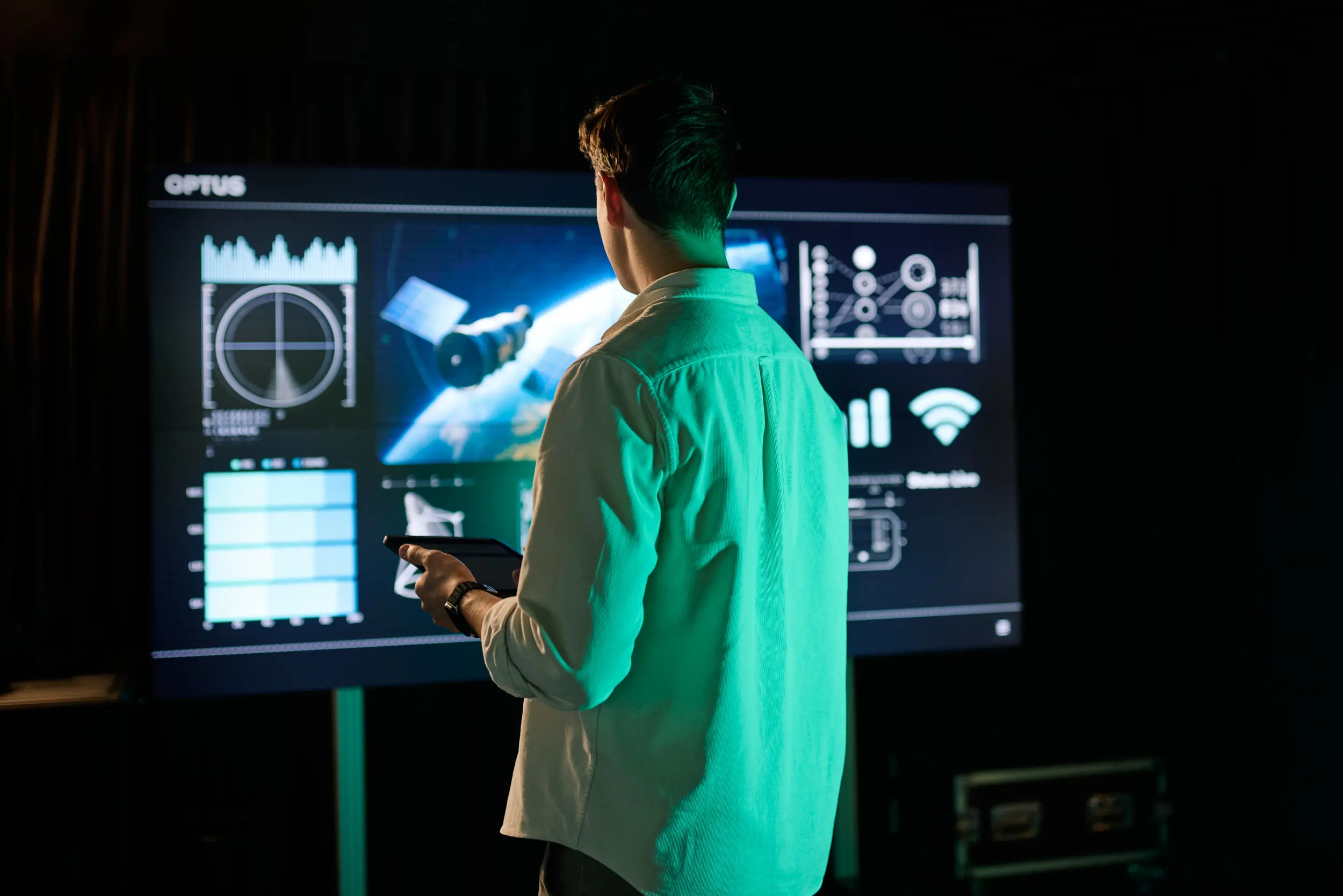 A man holding a smart tablet looking and computer display of a spacecraft
