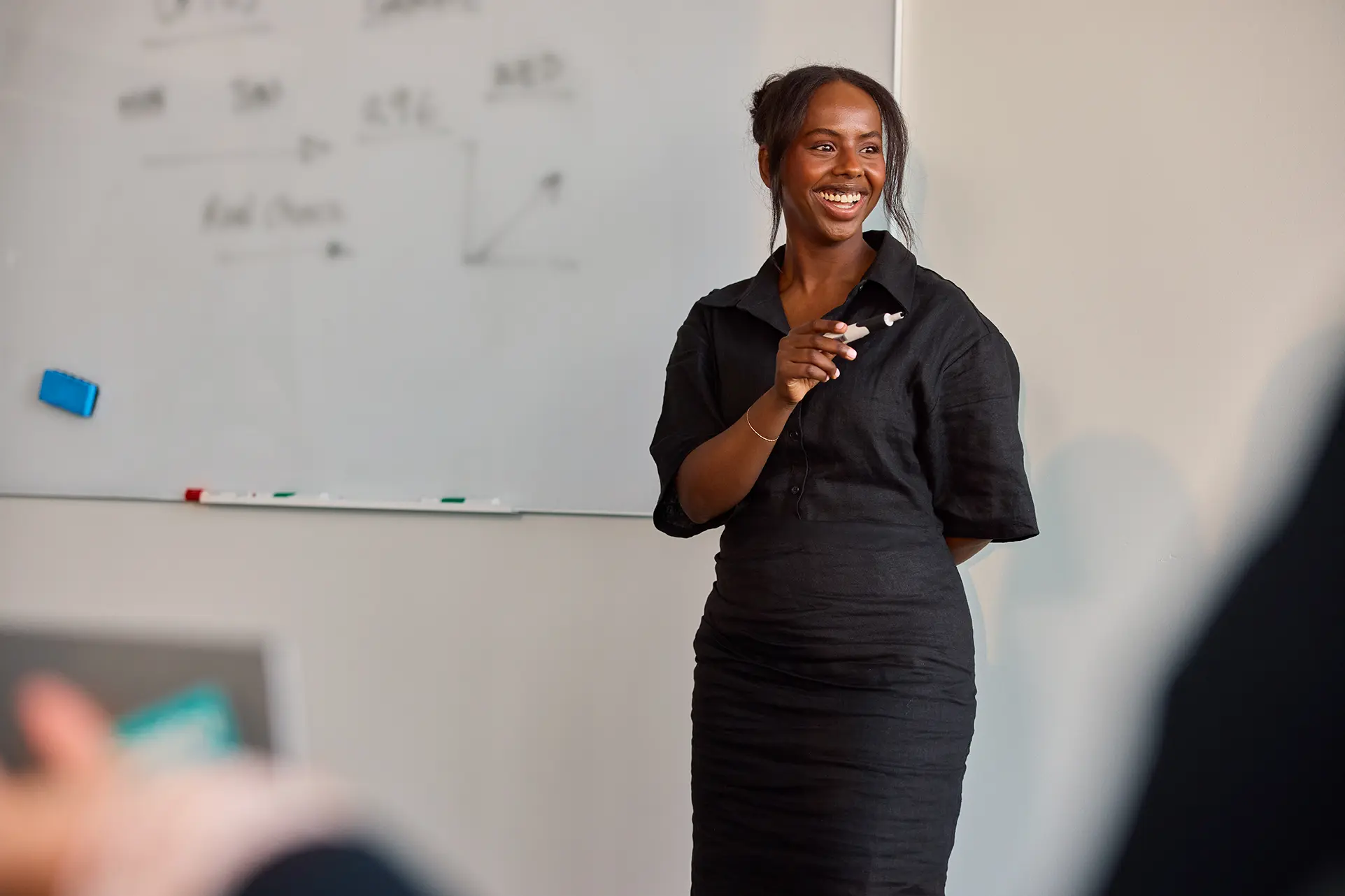 A woman holding a marker smiles and stands in front of a white board
