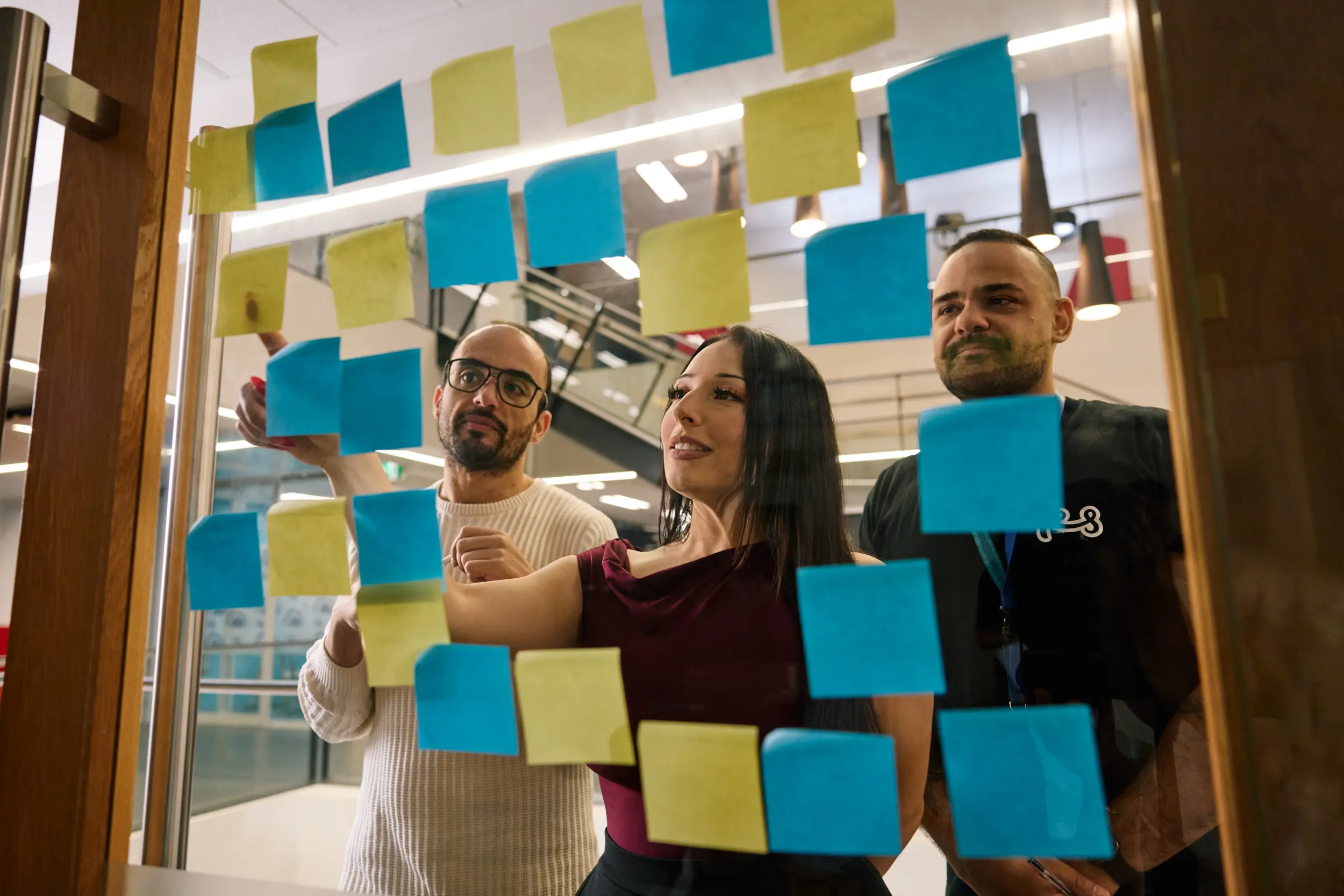 A group of people arrange post it notes and clear glass door