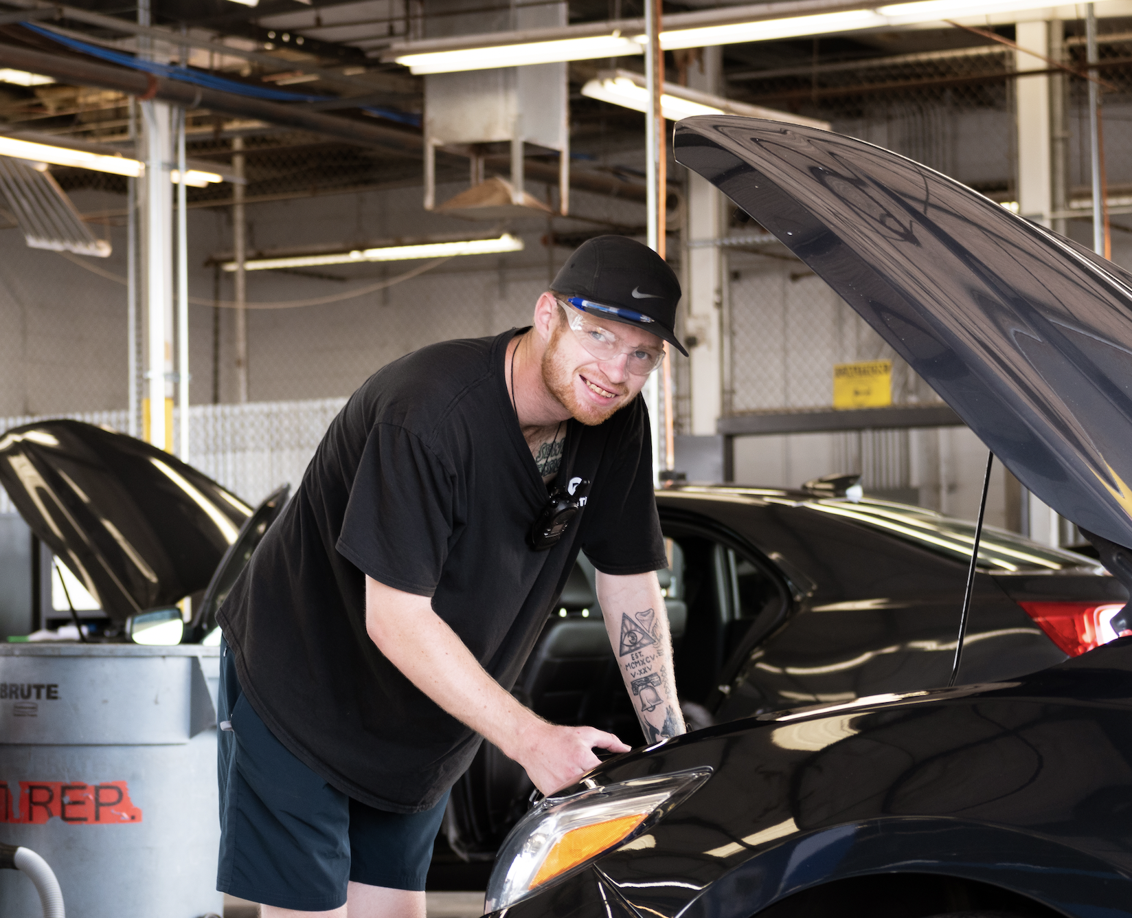 Happy male employee fixing the hood of a car