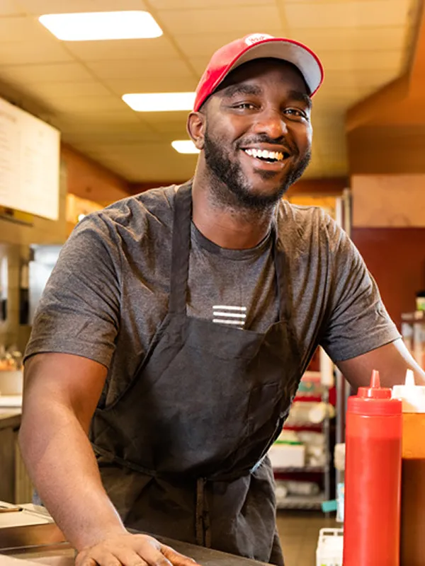 Smiling restaurant worker wearing apron and cap, representing competitive pay and future security.