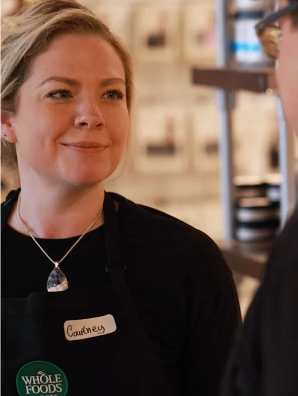 Whole Foods Market employee Courtney smiling while possibly talking to a colleague, representing the Team Member Assistance Program.