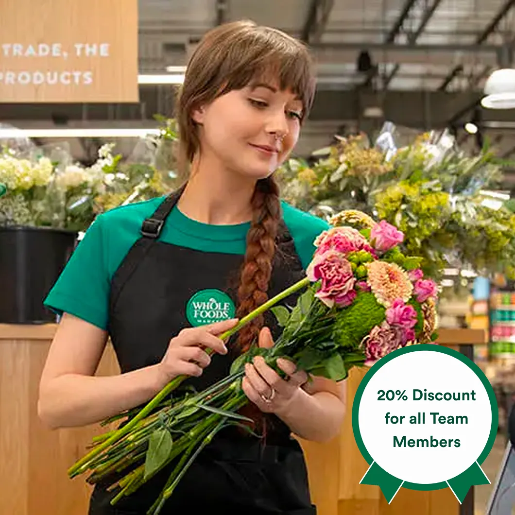 Whole Foods Market employee holding a bouquet of flowers with a 20% discount for team members badge.