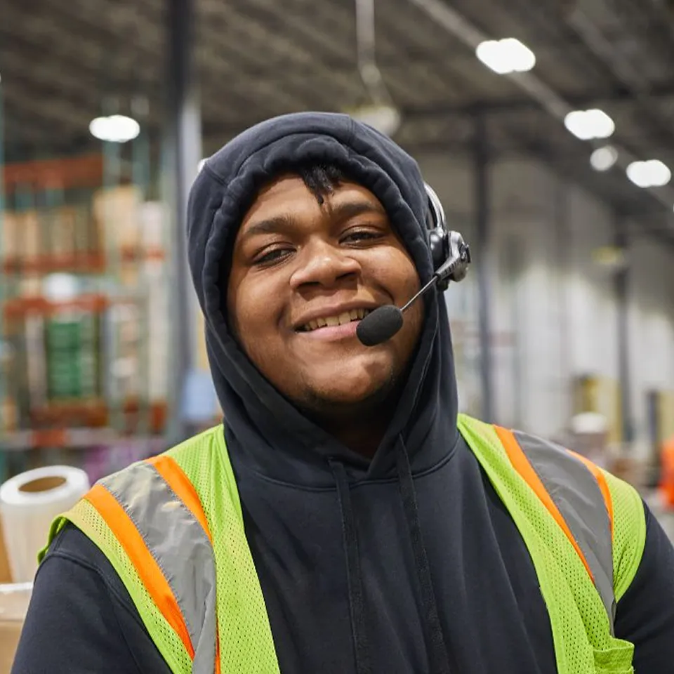 Jaylan, distribution center trainer, smiling wearing headset and safety vest