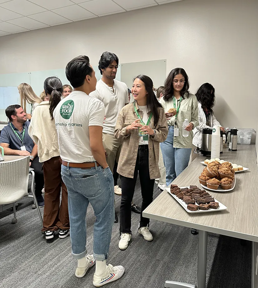 Group of people networking at a Whole Foods event with refreshments including brownies and muffins.
