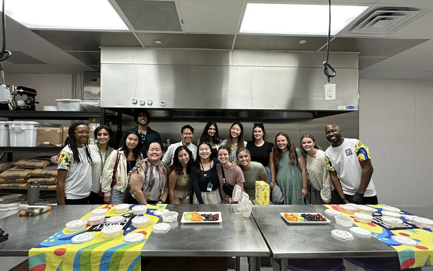 Group of diverse people smiling in a kitchen setting with prepared food on a table.