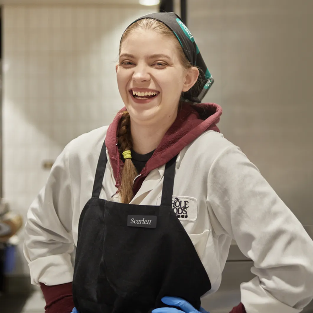 Smiling Whole Foods Market apprentice Scarlett wearing apron and head covering.