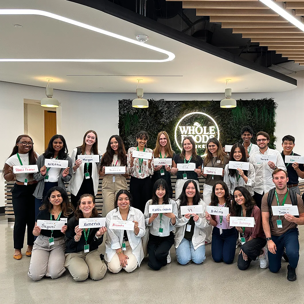 Whole Foods Market interns holding name cards in front of Whole Foods Market logo.