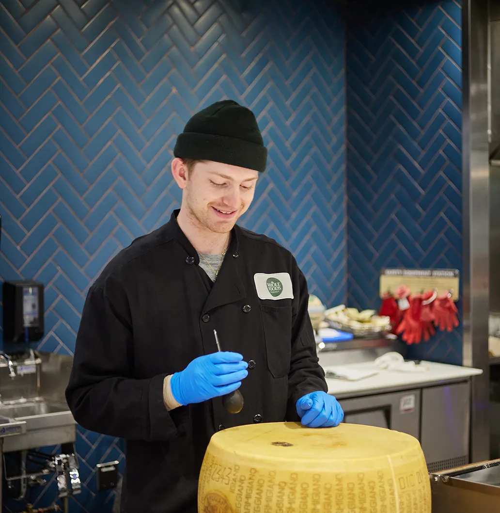 Whole Foods employee cutting a wheel of Parmigiano Reggiano cheese.