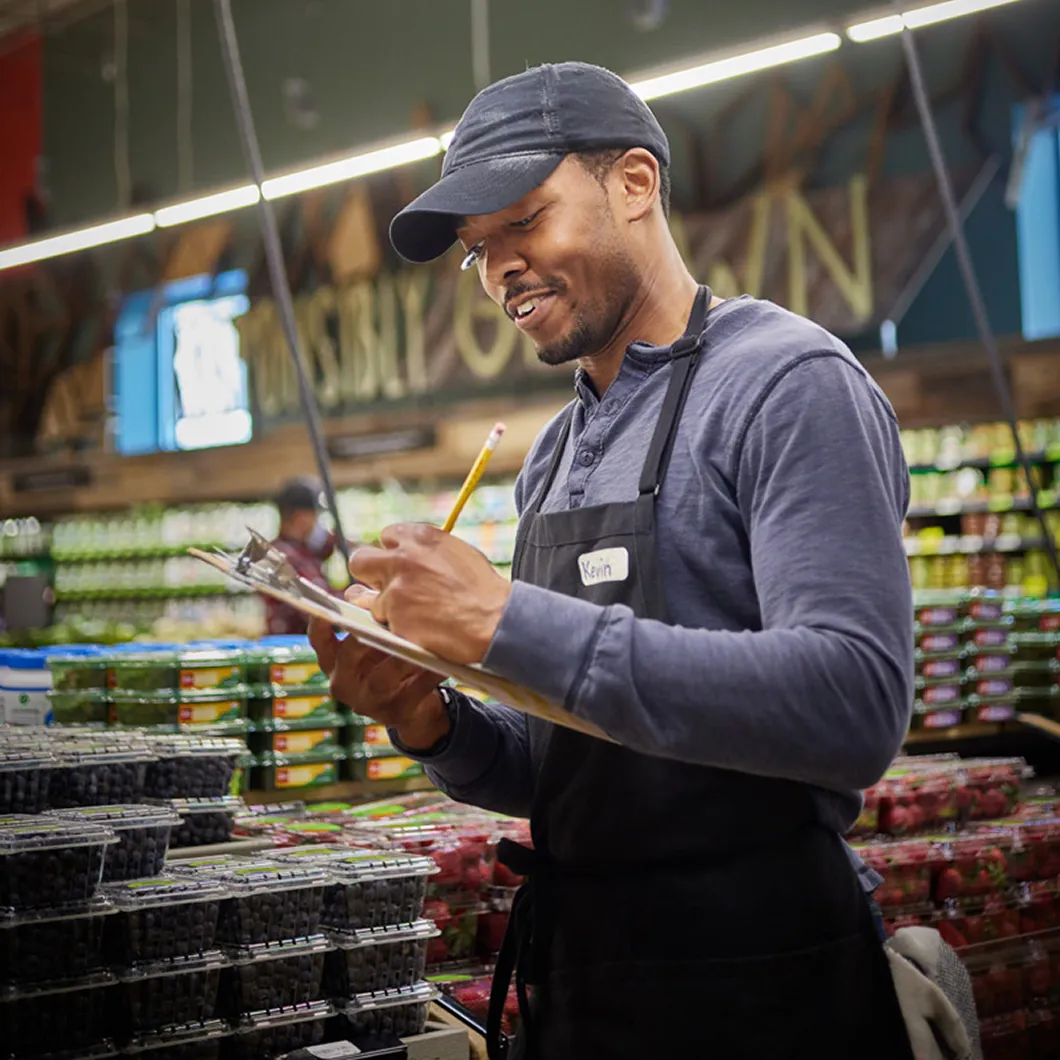 Whole Foods Market employee writing on a clipboard in a grocery store aisle